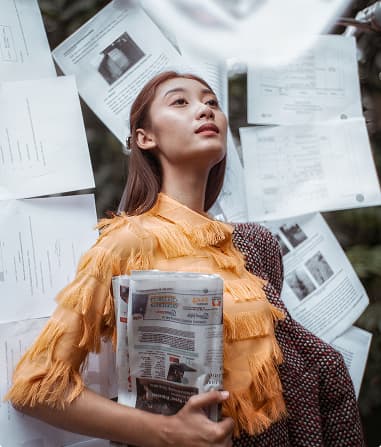 Fashion model in yellow ruffled top surrounded by flying newspapers