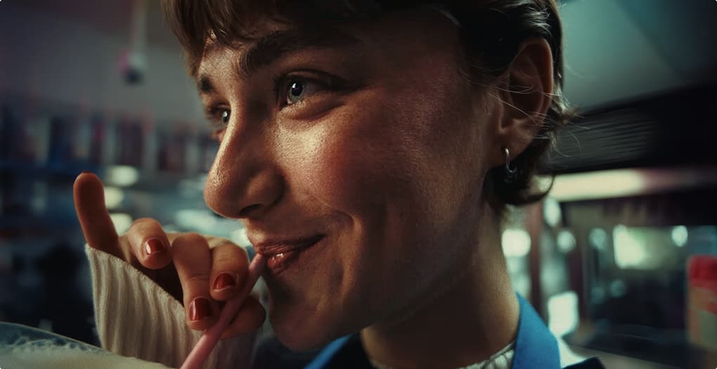 Close-up profile of a smiling woman drinking through a pink straw